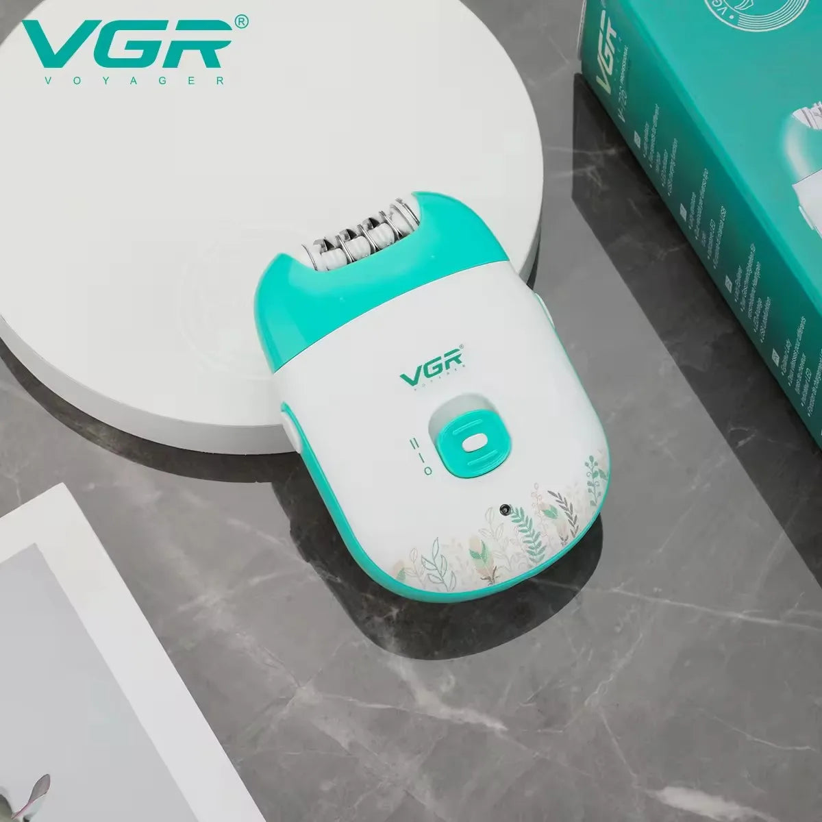 Perspective shot of the VGR V-726 white and green compact epilator resting on a stone display block next to its box