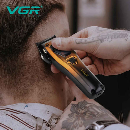 Close-up view of a tattooed barber's hands precisely operating the gold and black VGR Voyager hair clipper to trim the short hair on the back of a client's neck.