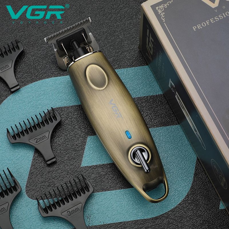 close up overhead shot of the vgr v-978 professional zero cut trimmer showing the antique gold metal body textured grip blue led indicator light premium on off toggle switch and stainless steel t blade next to black plastic guide combs and product packaging box